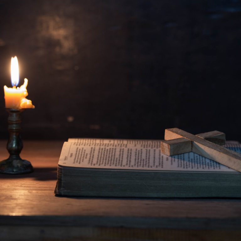 Wood cross laying on an opened Bible, with candle and candlelight on table